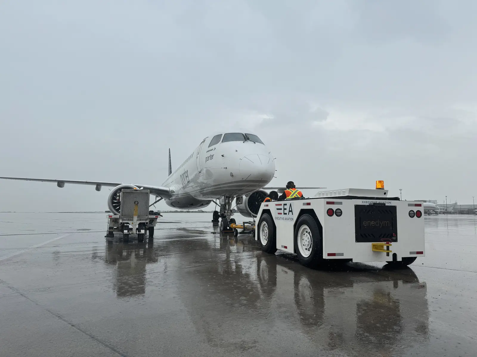Enedym-converted electric pushback tractor towing a Porter Embraer E195 on a wet apron